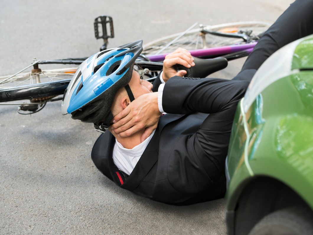 cyclist with a blue helmet holding his neck on the ground