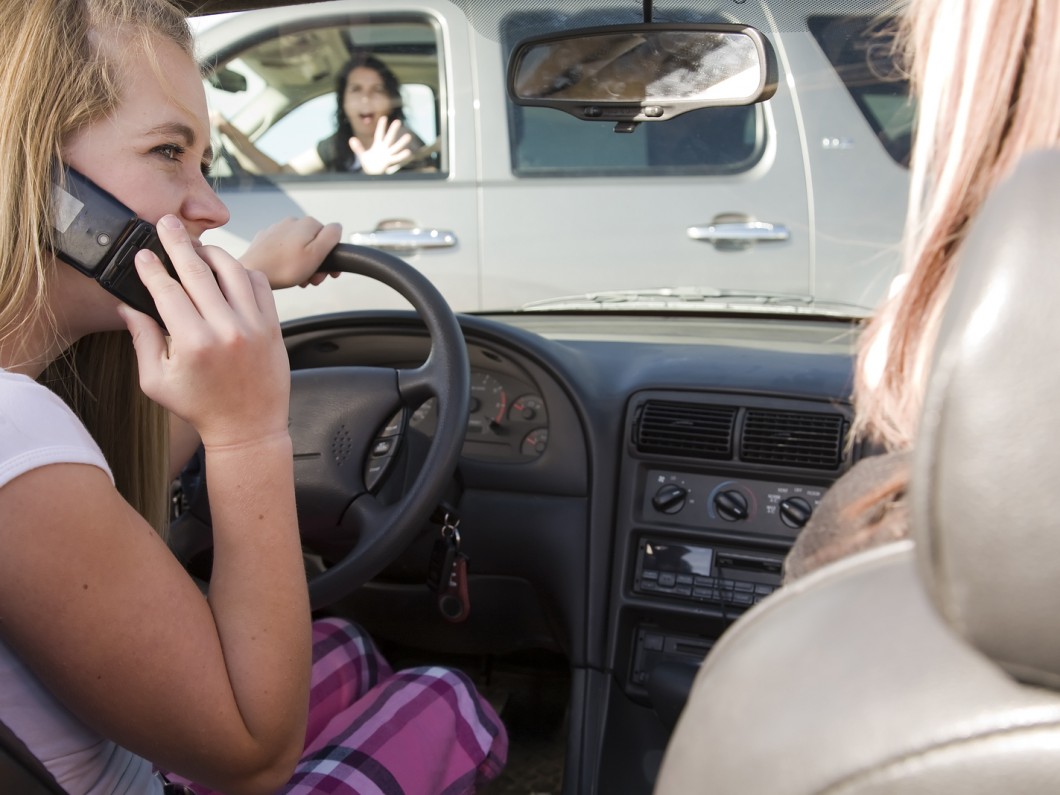 young girl on cellphone talking to passenger about to crash into another car