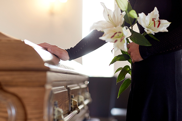 person dressed in black touching a wooden coffin